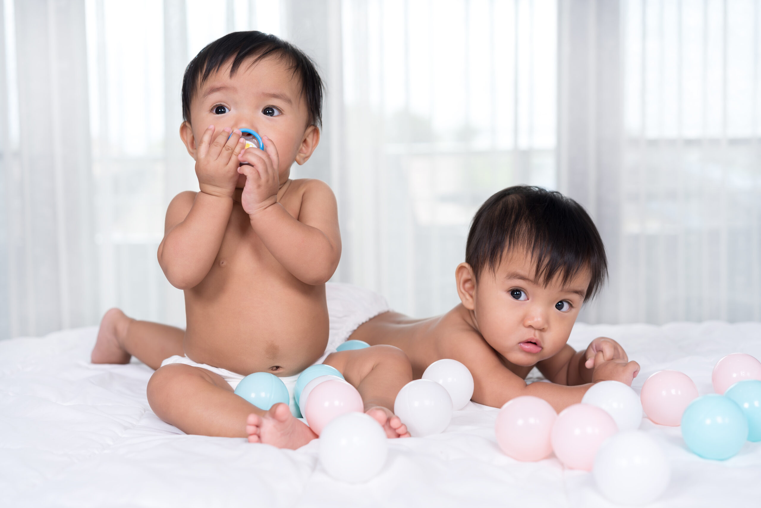 twin babies on a bed with balls